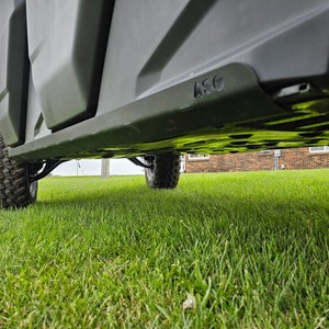 May include: Underside view of a black off-road vehicle with a black plastic skid plate. The skid plate has the letters "ASG" embossed on it. The vehicle is parked on a grassy lawn.