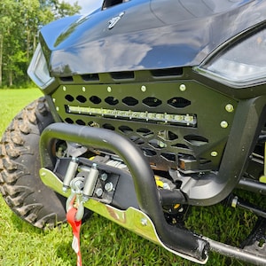 May include: Black off-road vehicle with a black metal grille and a light bar. The vehicle has a black bumper with a silver tow hook and a red tow strap.