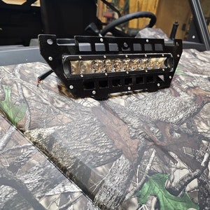 May include: A black metal light bar with a row of LED lights mounted on a camouflage-patterned surface.