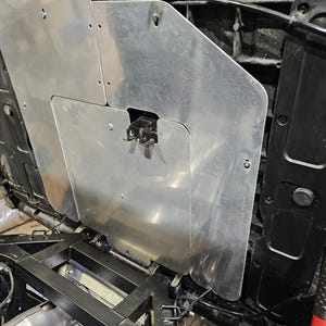 May include: Aluminum metal paneling installed on a vehicle. The panels are silver and have a brushed finish. The image shows the underside of the vehicle's hood, with the panels covering the engine compartment. Fasteners and a latch are visible.