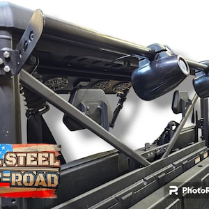 May include: A black metal roll cage with two black speakers mounted on top. The roll cage is attached to a black vehicle. The words "ALL STEEL OFF-ROAD" are visible on the side of the vehicle.