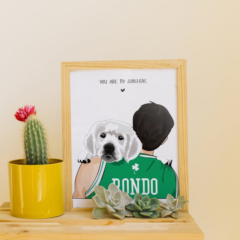 May include: A framed illustration of a person wearing a green and white jersey with the word "Rondo" on it. The person is holding a white dog with black eyes and a black nose. The text "You are my sunshine" is at the top of the frame.