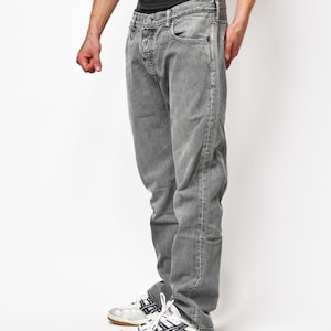 May include: A pair of grey denim jeans with a button fly closure and a classic five-pocket design. The jeans feature a faded wash, visible stitching along the seams, and a straight-leg cut. The waistband is worn low, revealing black underwear.