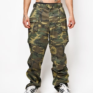 Könnte beinhalten: Cargohose mit Camouflage-Muster und Reißverschluss-Design, das die Hose in Shorts verwandelt. Die Hose verfügt über mehrere Utility-Taschen an den Oberschenkeln, einen Knopf- und Reißverschluss sowie Gürtelschlaufen im klassischen Wald-Tarnmuster.