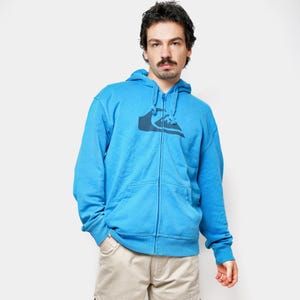 以下が含まれることがあります： 胸にロゴが入ったライトブルーのジップアップパーカーとベージュのカーゴパンツを着た人。パーカーにはフードとフロントポケットが付いています。パンツには複数のポケットがあり、ゆったりとしたフィット感です。カジュアルな服装です。