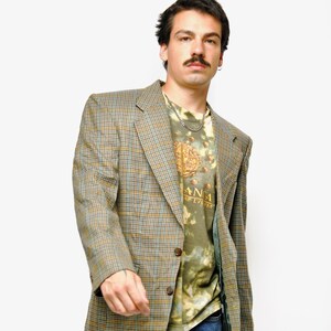 May include: A vintage-style blazer in a plaid pattern of brown, blue, and yellow. The blazer is worn over a green tie-dye t-shirt and blue jeans. The t-shirt has the text "ANA" on it.