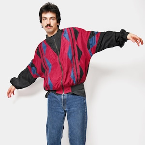 以下が含まれることがあります： ジッパー開閉の、赤、黒、青の幾何学模様のヴィンテージジャケット。 ジャケットは黒い袖で、青いジーンズと黒いスニーカーと組み合わせています。 この服装はレトロスタイルです。