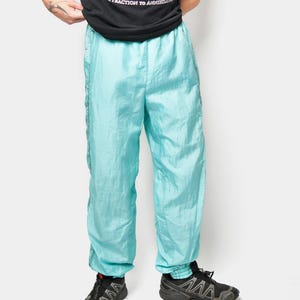 May include: A person wearing a black t-shirt with the word "MALLENER" and a graphic design. They are also wearing light blue nylon track pants and black athletic shoes.