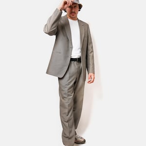 May include: A man wearing a gray suit with a white t-shirt and a gray bucket hat. He is wearing white sneakers with red accents.