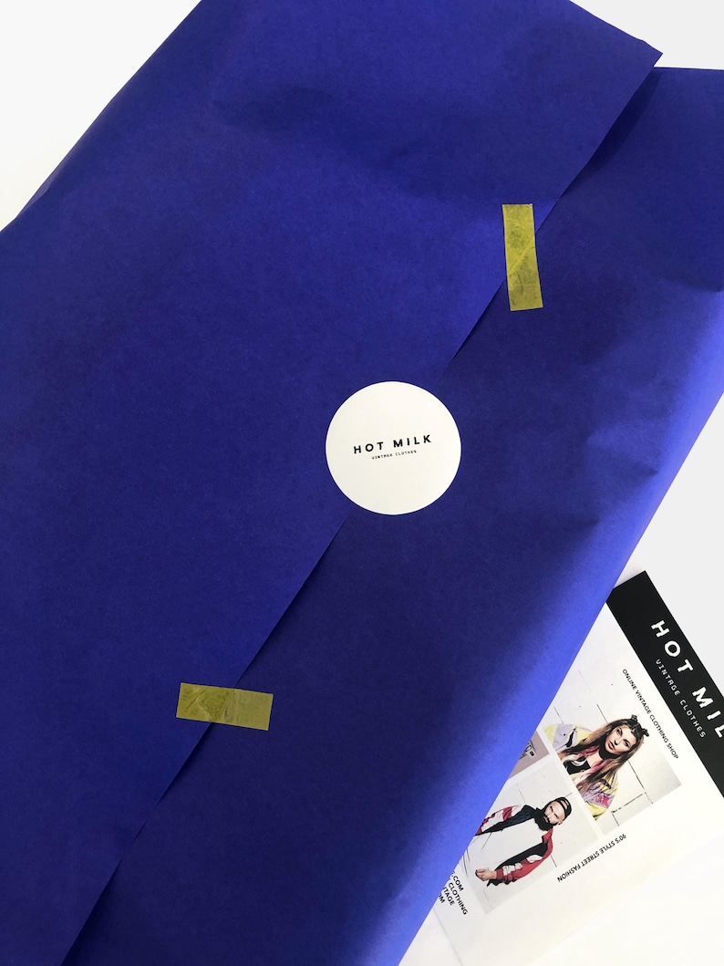 May include: A package wrapped in deep blue paper, sealed with gold tape and a white circular sticker with the text "HOT MILK VINTAGE CLOTHES". A promotional card with the text "HOT MILK ONLINE VINTAGE CLOTHING SHOP" is visible.