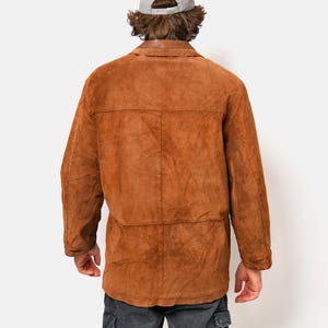 May include: A brown suede jacket with a long sleeve and a button closure. The jacket has a relaxed fit and a casual style.