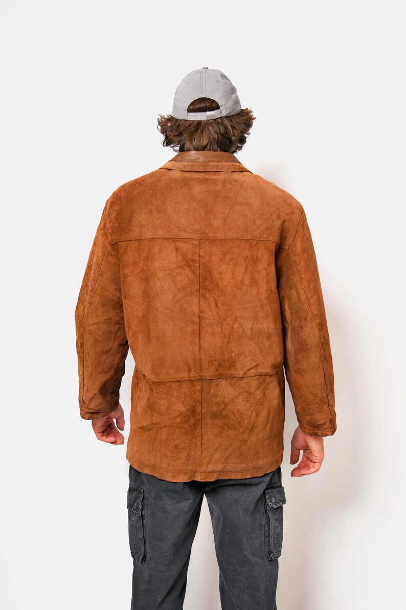 May include: A brown suede jacket with a long sleeve and a button closure. The jacket has a relaxed fit and a casual style.