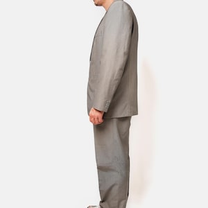 May include: A gray suit with a matching gray cap. The suit jacket has a single button closure and the pants have a straight leg. The person is wearing white sneakers with red accents.