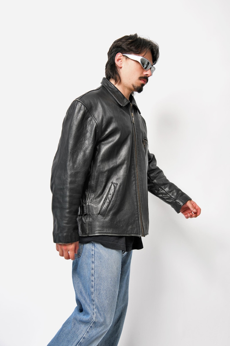 以下が含まれることがあります： ジッパー留めとスタンドカラーの黒い革のジャケット。ジャケットには前面にポケットが2つとウエストにベルトが付いています。