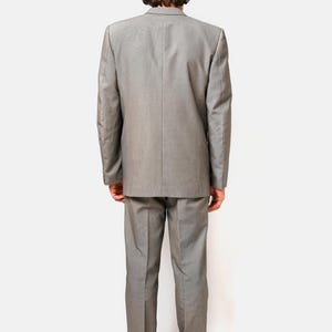 May include: A gray suit with a matching jacket and pants. The person is wearing a gray baseball cap.
