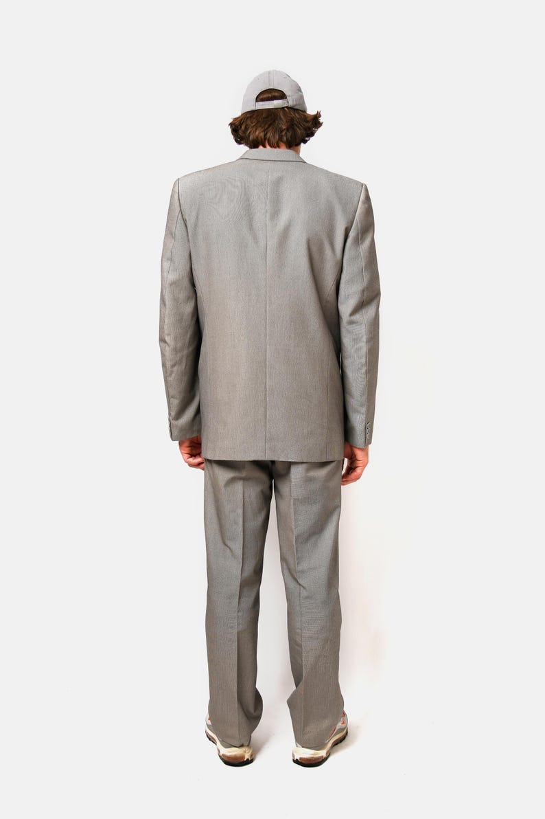 May include: A gray suit with a matching jacket and pants. The person is wearing a gray baseball cap.