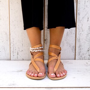 May include: Tan leather sandals with multiple straps and a white beaded ankle bracelet.