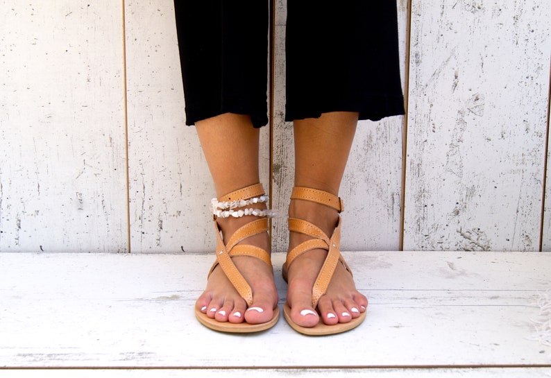 May include: Tan leather sandals with multiple straps and a white beaded ankle bracelet.
