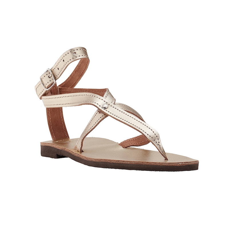 May include: Gold leather sandals with a buckle closure and multiple straps. The sandals have a flat sole and a comfortable design.