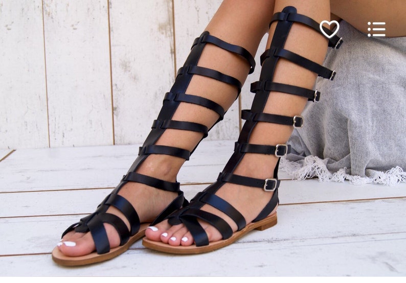May include: Black leather gladiator sandals with multiple straps and buckles. The sandals have a flat sole and reach above the ankle.