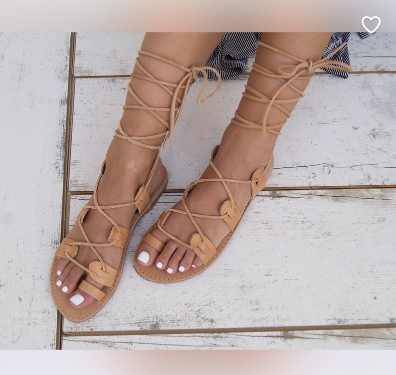 May include: Tan leather sandals with laces that tie up the leg. The sandals have a simple design with a rounded toe.