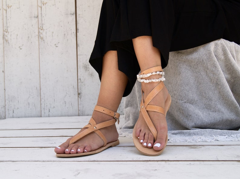 May include: A pair of tan leather sandals with ankle straps and a buckle closure. The sandals have a simple design and are perfect for summer.