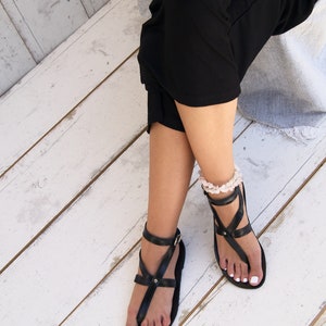 May include: A pair of black leather sandals with ankle straps and buckles. The sandals have a simple design and are perfect for summer.