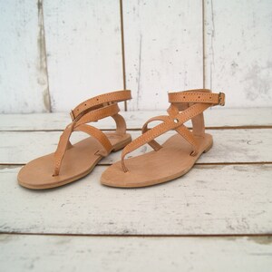 May include: A pair of tan leather sandals with multiple straps and buckles. The sandals have a flat sole and are made of a soft, supple leather.