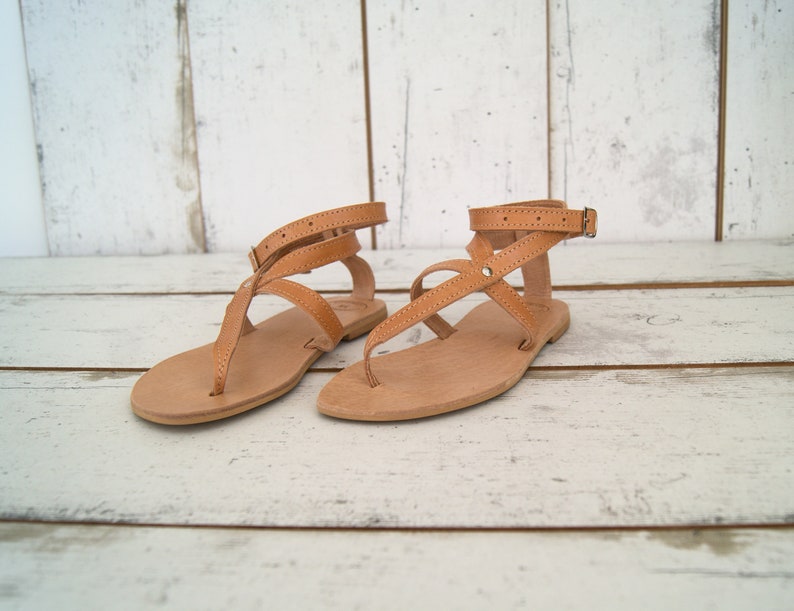 May include: A pair of tan leather sandals with multiple straps and buckles. The sandals have a flat sole and are made of a soft, supple leather.