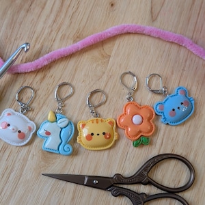 Peut inclure: Cinq marqueurs de points de crochet colorés avec des motifs d'animaux et de fleurs. Les marqueurs sont attachés à des anneaux argentés. Les marqueurs sont un ours blanc, une licorne bleue, un poussin jaune, une fleur orange et un ours bleu.