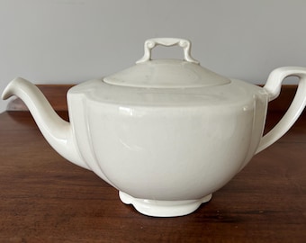May include: A white ceramic teapot with a lid and a handle. The teapot has a rounded body and a slightly flared spout.