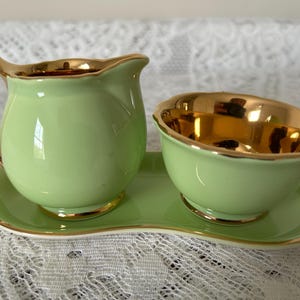 Könnte beinhalten: Ein Vintage-Set aus grüner Keramik-Sahne- und Zuckerdose mit goldenen Verzierungen. Der Sahnebereiter hat einen gebogenen Griff und einen Ausguss. Die Zuckerdose ist rund. Beide stehen auf einem passenden Tablett. Ein klassisches Teeservice.