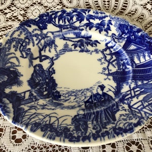 Könnte beinhalten: Ein blauer und weißer Keramikteller mit japanisch inspiriertem Design. Der Teller zeigt eine Pagode, Bäume und Figuren in einer Landschaft.