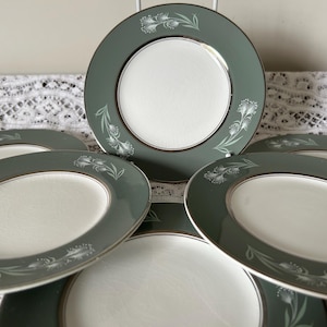 Puede incluir: Un juego de seis platos vintage. Cada plato presenta un centro blanco, un borde verde salvia con ribete plateado y un delicado diseño floral. Los platos tienen aproximadamente 20 cm de diámetro.