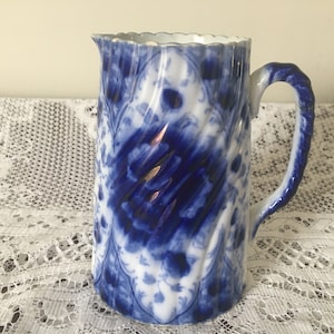 May include: A blue and white ceramic jug with a swirling pattern and a handle. The jug has a white background with a blue floral design.