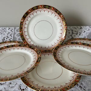 Puede incluir: Juego de cuatro platos de cerámica vintage con un diseño floral y dorado. Los platos tienen un fondo blanco con un patrón floral rojo, dorado y verde alrededor del borde.