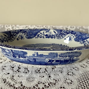 May include: Oval ceramic serving dish with a blue and white landscape and floral design. The dish has a scalloped edge and a detailed pattern around the rim. The interior features a scenic illustration of a building, trees, and water.