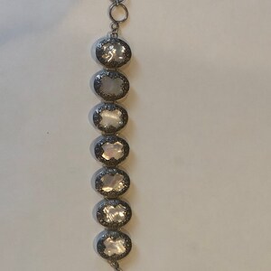 May include: Silver-toned bracelet featuring seven oval, iridescent mother-of-pearl stones. Each stone is framed by a decorative, ornate silver setting. The bracelet has a toggle clasp and a series of connecting rings at the top.