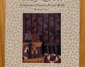 以下が含まれることがあります： リネット・ジェンセン著「Cozy Quilts: A Collection of Country Flannel Quilts」というタイトルの本。表紙には、青、赤、白の色のパッチワーク模様のキルトが描かれている。この本はシンブルベリー社から出版されている。