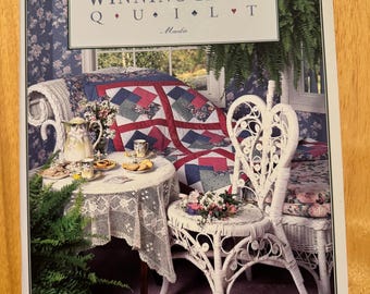 以下が含まれることがあります： 「Winning Hand Quilt」というタイトルの、表紙が青と白の花柄の書籍。白い籐製の椅子とソファが載っており、ソファには赤、青、白のキルトがかけられている。この書籍は「Quilt in a Day」シリーズの一部である。