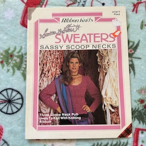 May include: A vintage book cover for "Sweaters" by Susan Starr, featuring a woman in a pink scoop-neck sweater. The cover has a pink and white border with the text "Ribbon Knits" and "Sassy Scoop Necks". The book is about knitting.