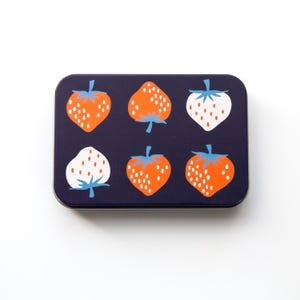 May include: A rectangular, navy blue tin with a repeating pattern of stylized strawberries. The strawberries are orange and white with blue stems and leaves. The tin is likely used for storage or as a decorative item.