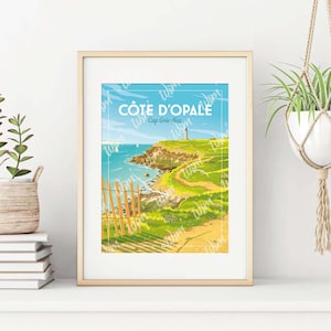 Op de afbeelding: Een ingelijste prent met een kustlandschap met de tekst "CÔTE D'OPALE Cap Gris-Nez". Het kunstwerk toont een vuurtoren op een klif, een pad en een houten hek. Het kleurenpalet omvat blauw, groen, geel en wit.