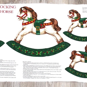 May include: White fabric panel featuring multiple illustrations of a rocking horse with a brown mane and tail, red bridle, and green saddle. The rocking horses are on a green base with holly accents. The words "ROCKING HORSE" are printed at the top.