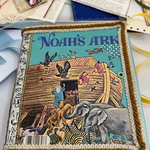May include: A vintage children's book titled "Noah's Ark" with a colorful illustration of animals entering the ark. The book has a teal cover with gold trim and decorative embellishments. The cover art depicts various animals, birds, and the biblical figure of Noah.