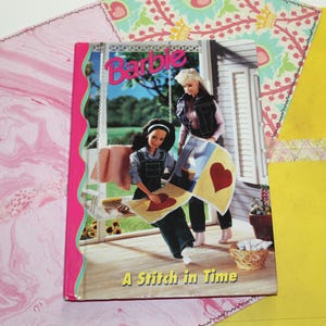 May include: A Barbie book titled "A Stitch in Time" with a pink cover and a picture of two Barbie dolls. One doll is sitting on a swing, and the other is standing. The background shows a porch and a sunny day.