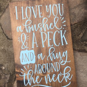 May include: A wooden sign with the text "I love you a bushel & a peck and a hug around the neck" in light blue lettering.