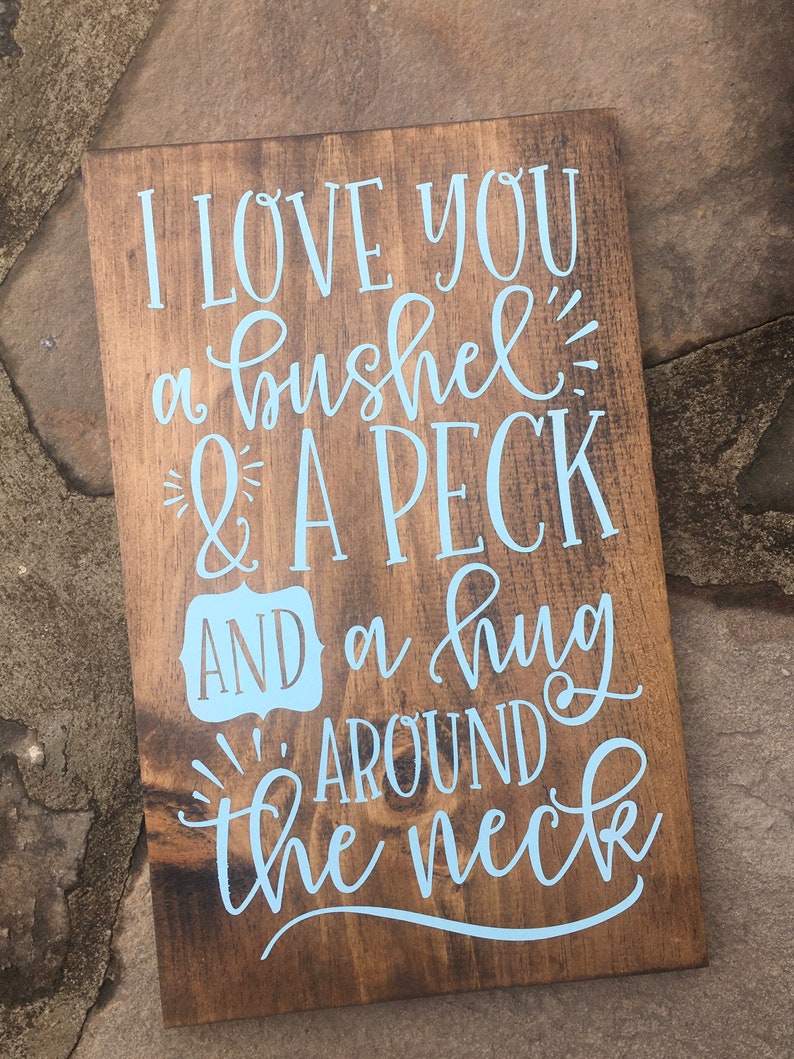 May include: A wooden sign with the text "I love you a bushel & a peck and a hug around the neck" in light blue lettering.