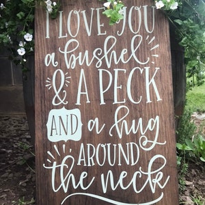 May include: A wooden sign with white lettering that reads "I love you a bushel & a peck and a hug around the neck".