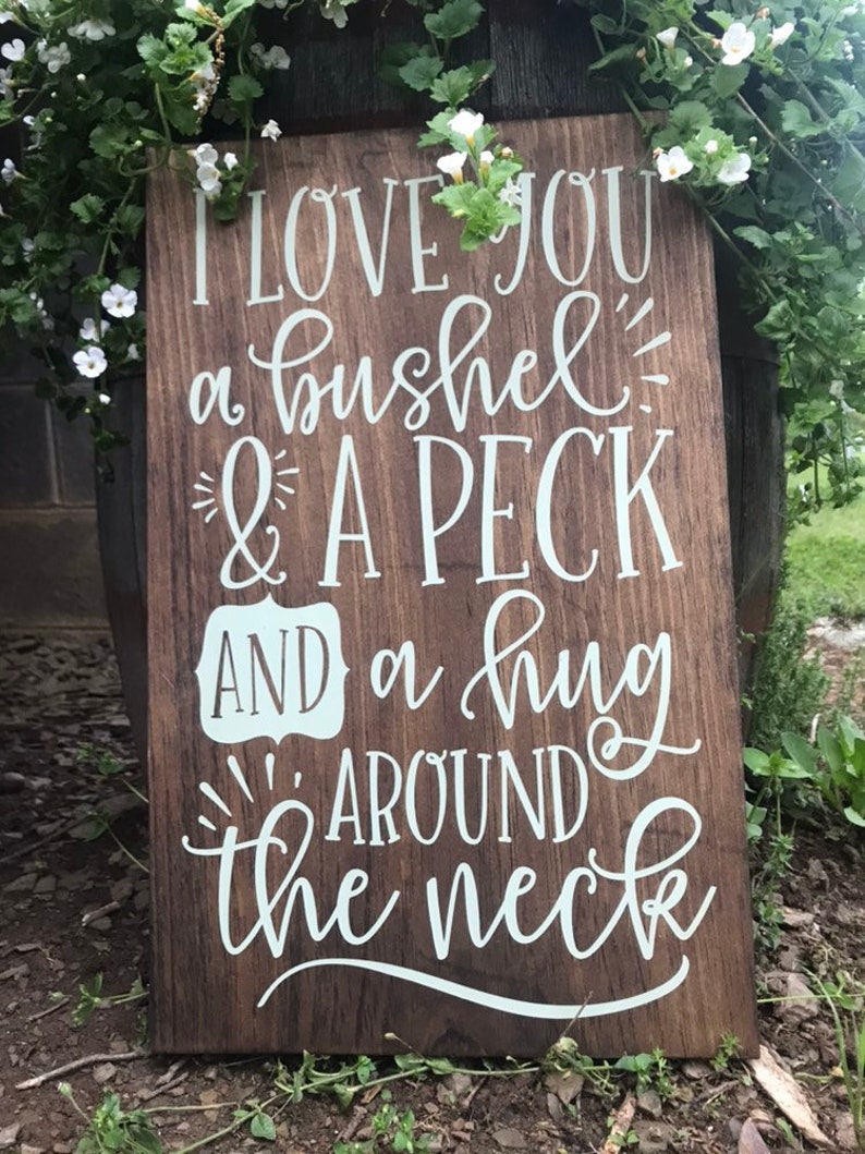 May include: A wooden sign with white lettering that reads "I love you a bushel & a peck and a hug around the neck".